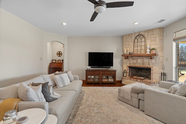 living area featuring arched walkways, a fireplace, wood finished floors, visible vents, and a ceiling fan