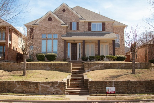 view of front of property featuring a shingled roof, stairs, and brick siding