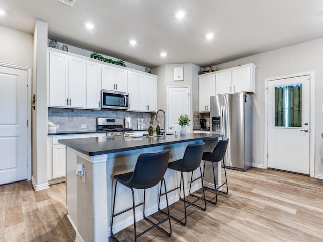 kitchen with dark countertops, a center island with sink, stainless steel appliances, and a sink