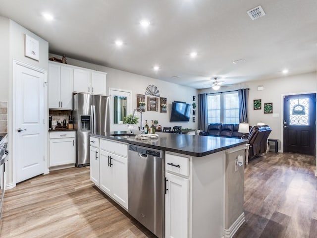 kitchen with light wood finished floors, appliances with stainless steel finishes, dark countertops, and a sink