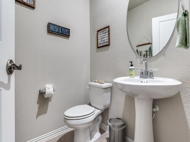 bathroom featuring baseboards, a textured wall, and toilet