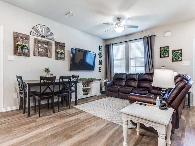 living room featuring ceiling fan, baseboards, visible vents, and light wood-style floors