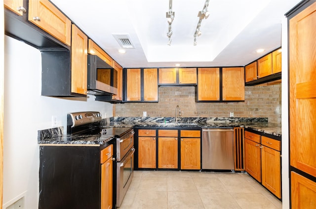 kitchen featuring a tray ceiling, visible vents, appliances with stainless steel finishes, a sink, and dark stone countertops