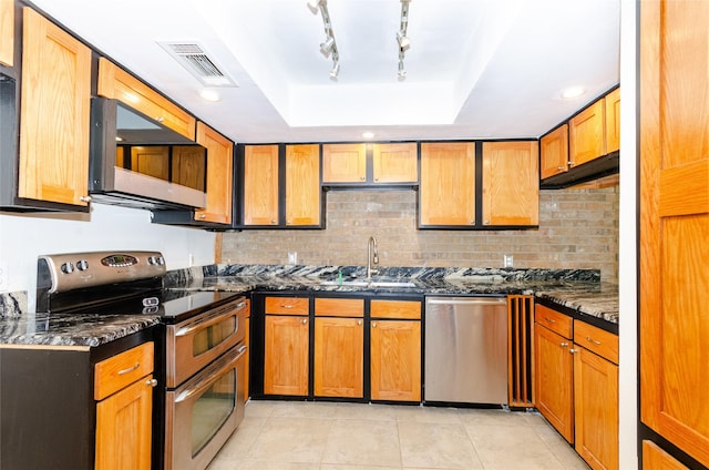 kitchen featuring visible vents, appliances with stainless steel finishes, brown cabinets, a tray ceiling, and dark stone countertops