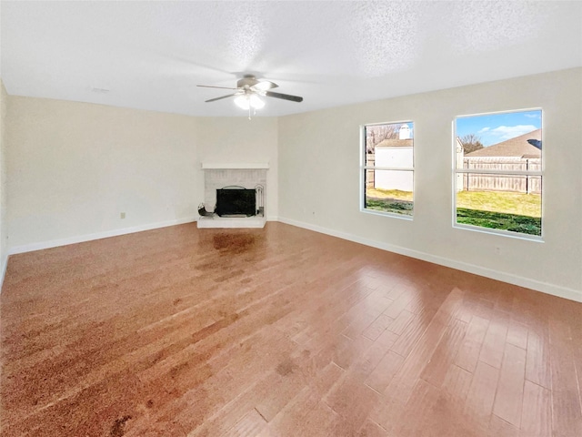 unfurnished living room featuring baseboards, ceiling fan, wood finished floors, a textured ceiling, and a fireplace