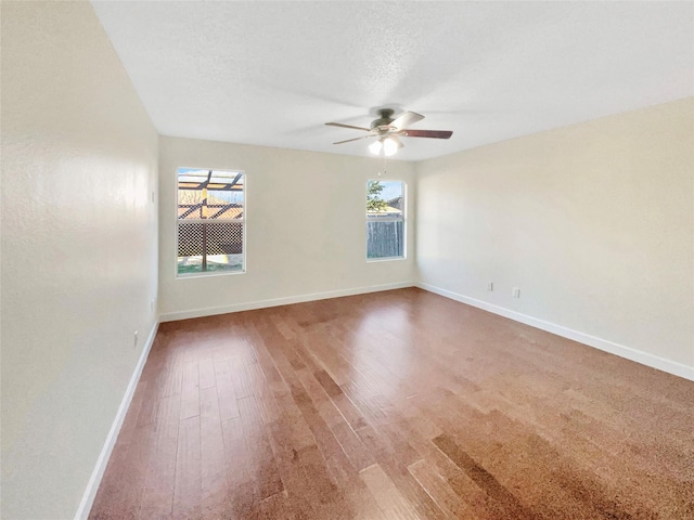 empty room with a textured ceiling, wood finished floors, a ceiling fan, and baseboards