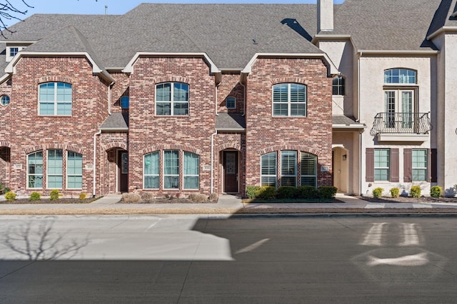 multi unit property with a shingled roof, a chimney, and brick siding