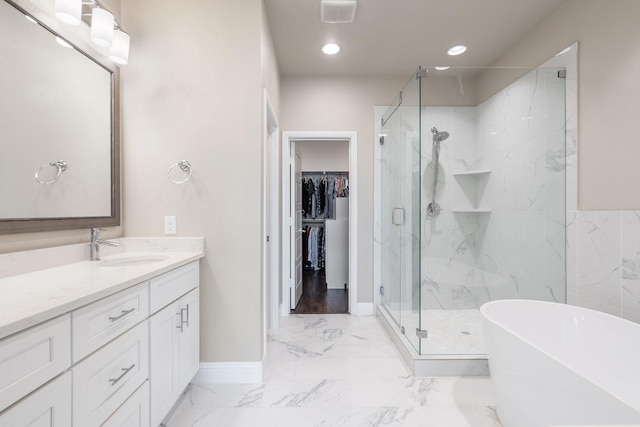 bathroom with marble finish floor, a marble finish shower, a spacious closet, vanity, and a freestanding tub