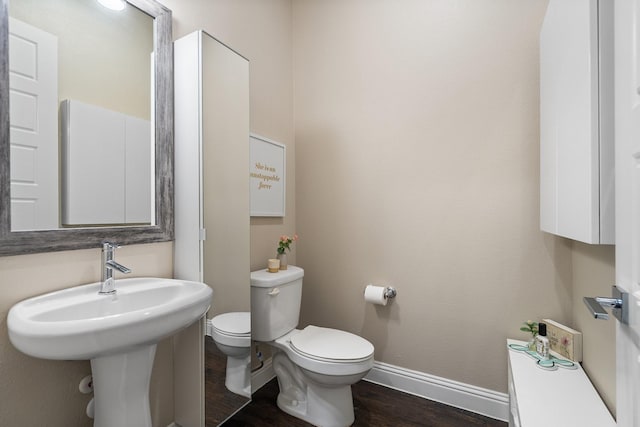 half bathroom featuring wood finished floors, toilet, and baseboards