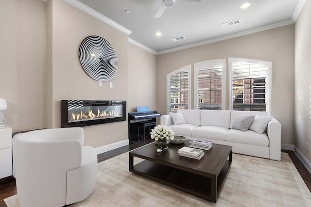 living room with crown molding, a glass covered fireplace, visible vents, and light wood-style floors