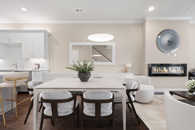 dining area with a glass covered fireplace, ornamental molding, dark wood-style flooring, stairs, and recessed lighting