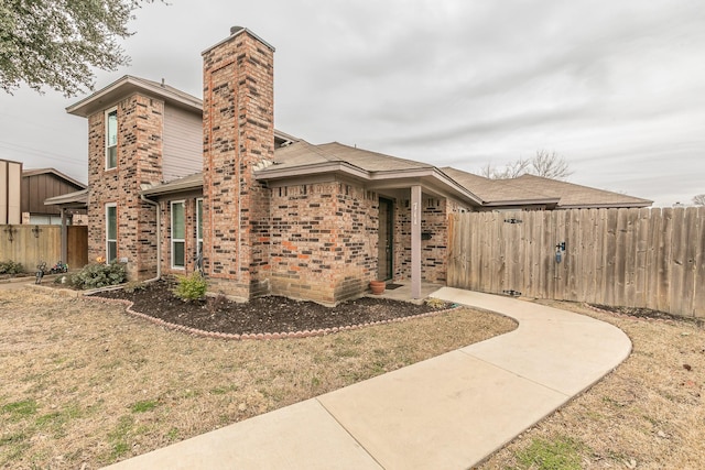 view of front facade with brick siding, a front lawn, and fence