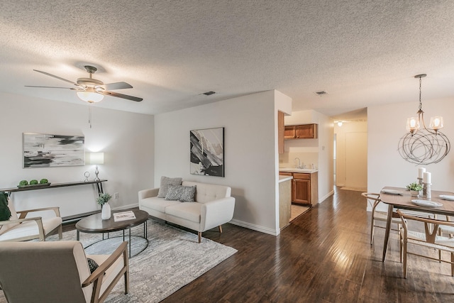 living area with ceiling fan with notable chandelier, dark wood-type flooring, visible vents, and baseboards