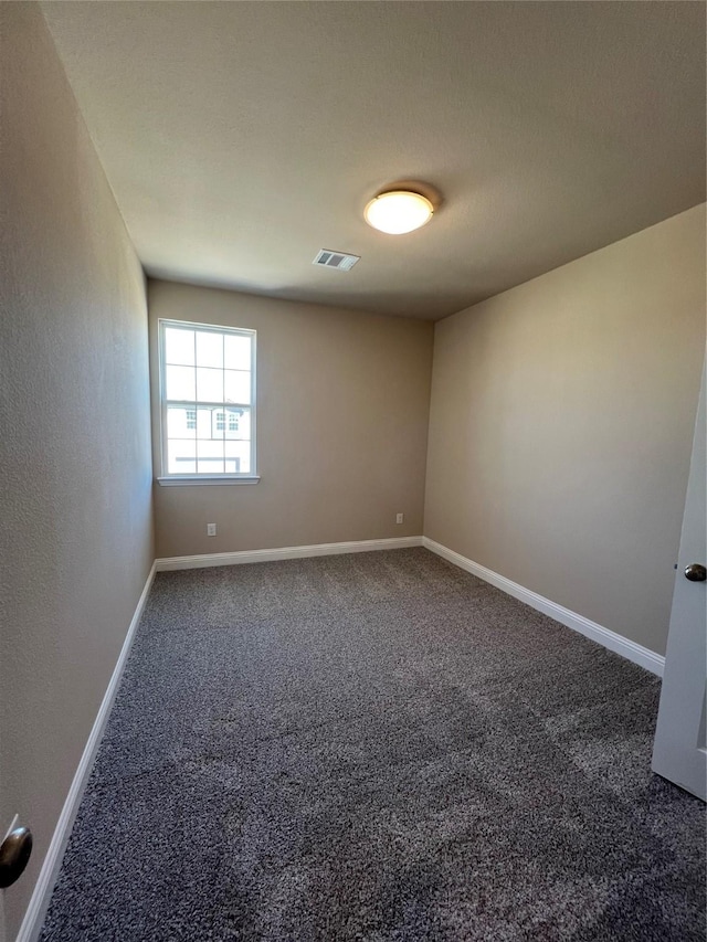 spare room featuring dark carpet, visible vents, and baseboards