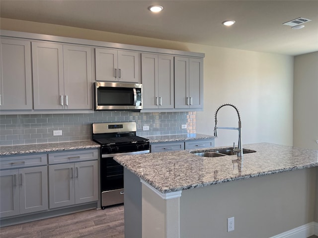 kitchen with a kitchen island with sink, stainless steel appliances, a sink, and visible vents