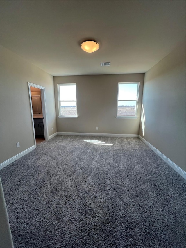 unfurnished bedroom featuring baseboards, multiple windows, visible vents, and dark colored carpet