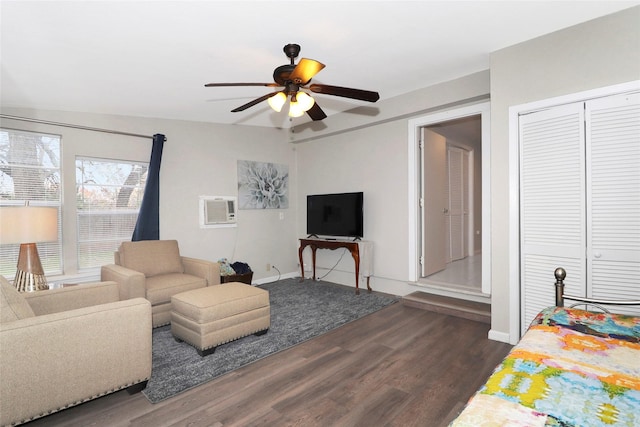 living area with dark wood-style floors, a wall unit AC, baseboards, and a ceiling fan