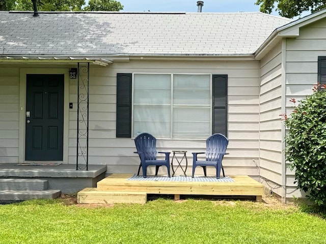 doorway to property with roof with shingles, a yard, and a deck