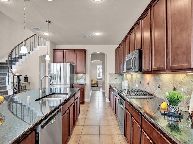 kitchen featuring visible vents, arched walkways, dark stone countertops, stainless steel appliances, and a sink