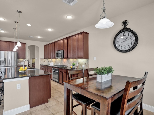 kitchen with arched walkways, stainless steel appliances, a sink, visible vents, and a center island with sink