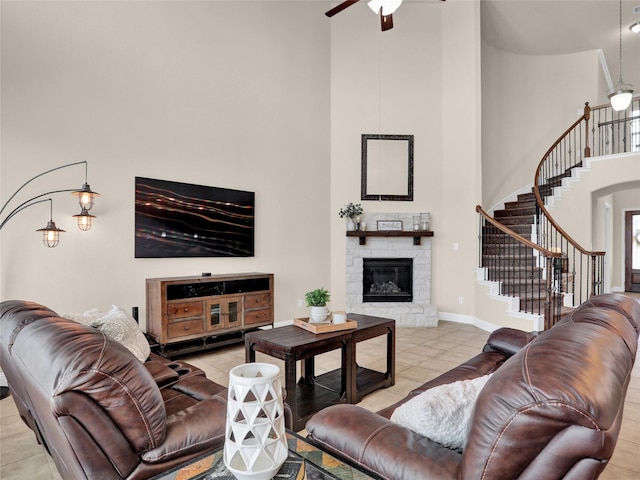 living area featuring a towering ceiling, ceiling fan, tile patterned flooring, stairs, and a fireplace