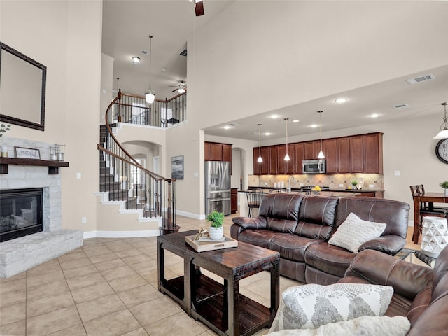 living room with light tile patterned floors, a stone fireplace, visible vents, baseboards, and stairs