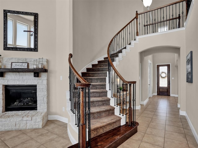 tiled foyer with arched walkways, a stone fireplace, a towering ceiling, and baseboards