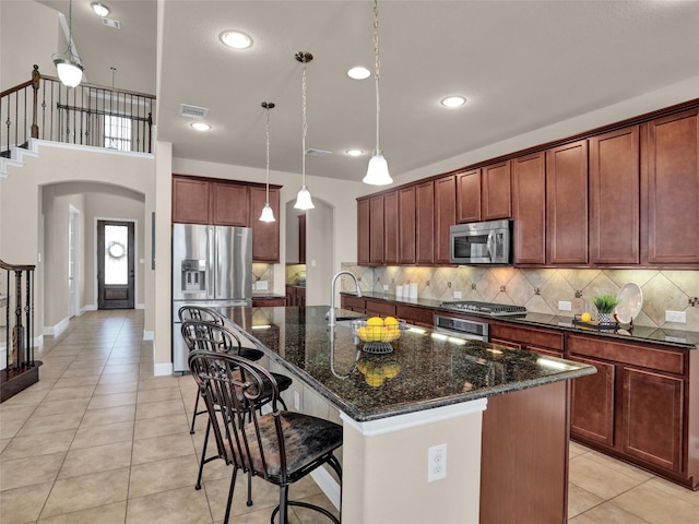 kitchen with arched walkways, stainless steel appliances, tasteful backsplash, and an island with sink