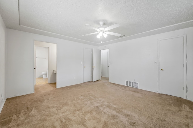 unfurnished bedroom with light carpet, a textured ceiling, connected bathroom, and visible vents