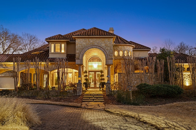 mediterranean / spanish house with french doors, a chimney, stucco siding, stone siding, and a tiled roof