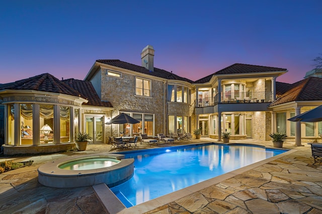 rear view of house with a balcony, a tiled roof, a pool with connected hot tub, and a patio