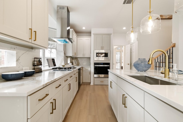 kitchen with appliances with stainless steel finishes, light stone counters, decorative light fixtures, wall chimney range hood, and a sink