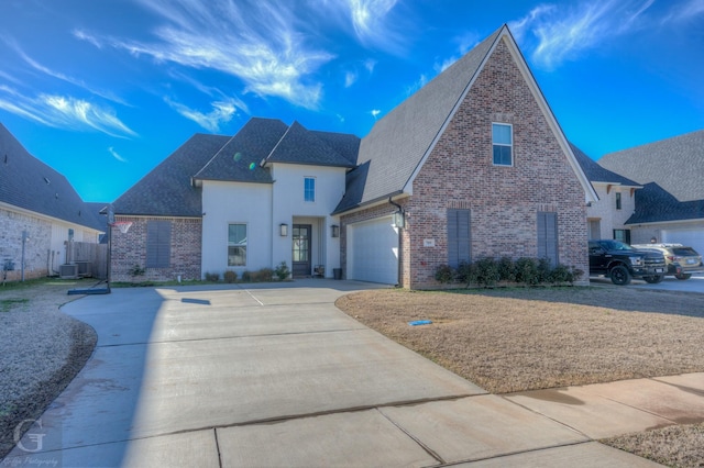 view of front of property featuring brick siding, roof with shingles, central AC unit, a garage, and driveway