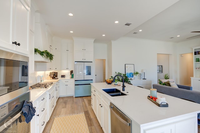 kitchen with a center island with sink, appliances with stainless steel finishes, light countertops, white cabinetry, and a sink