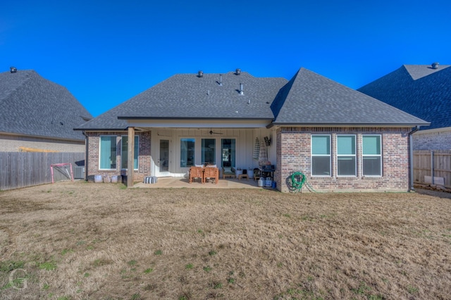 back of property with a fenced backyard, roof with shingles, and a patio