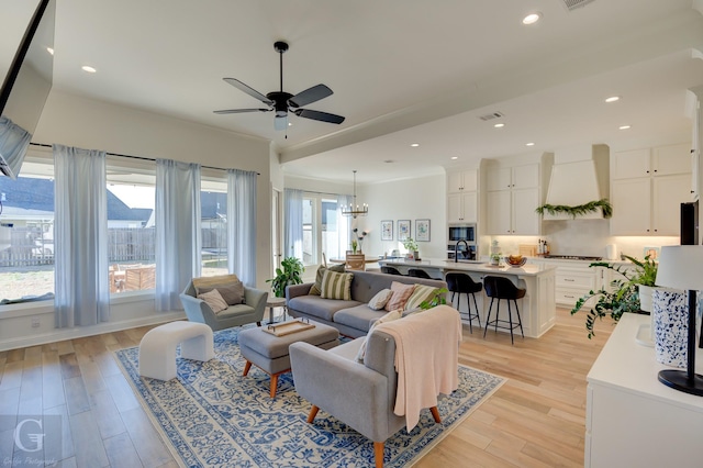 living room with light wood-style flooring, ceiling fan with notable chandelier, visible vents, and recessed lighting