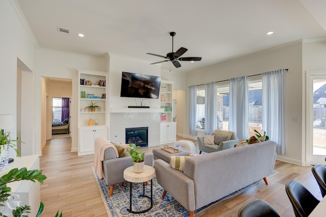 living room with visible vents, light wood-style floors, crown molding, a brick fireplace, and recessed lighting