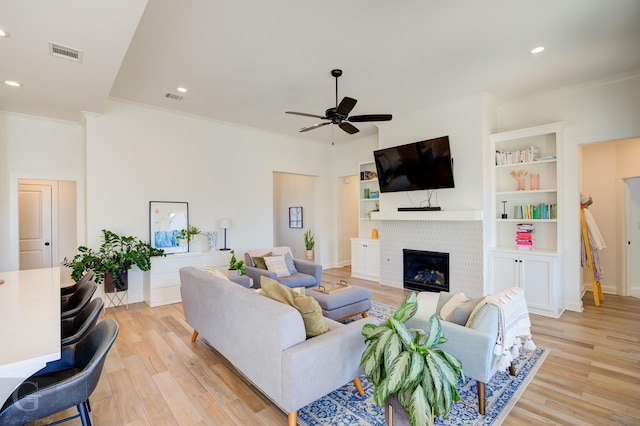 living area with a tiled fireplace, ceiling fan, light wood-type flooring, and visible vents