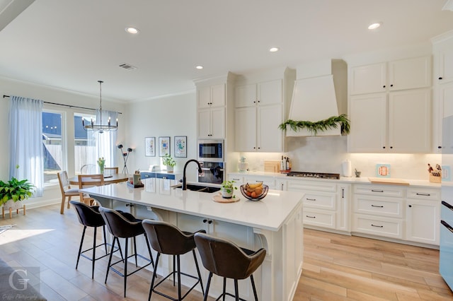 kitchen featuring premium range hood, a center island with sink, visible vents, and light countertops