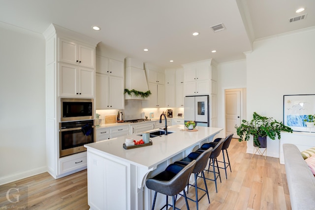 kitchen with stainless steel appliances, an island with sink, a sink, and white cabinets