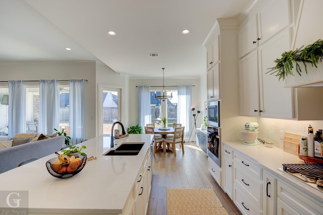 kitchen with a sink, white cabinetry, light countertops, appliances with stainless steel finishes, and a center island with sink