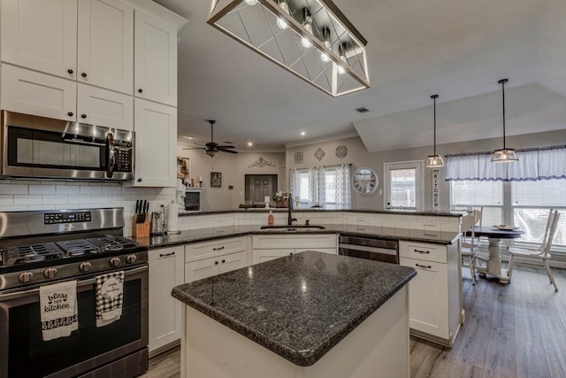 kitchen with stainless steel appliances, a peninsula, a sink, white cabinets, and decorative backsplash