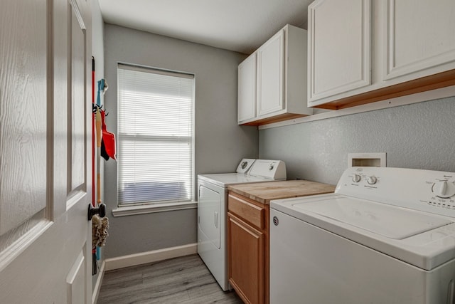 washroom featuring light wood finished floors, washing machine and clothes dryer, cabinet space, and baseboards