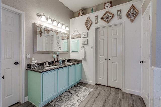 full bathroom featuring double vanity, a sink, baseboards, and wood finished floors