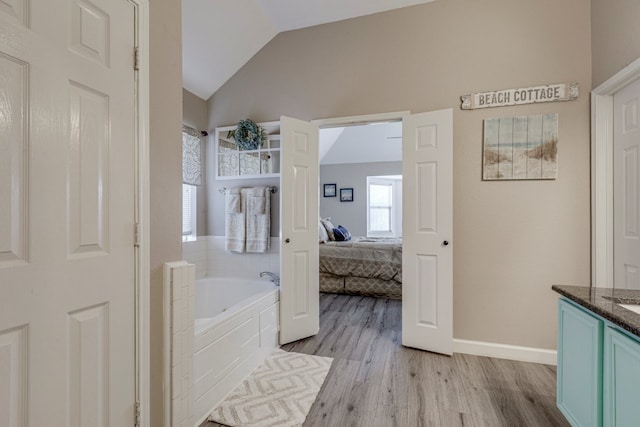 ensuite bathroom featuring a garden tub, lofted ceiling, connected bathroom, vanity, and wood finished floors