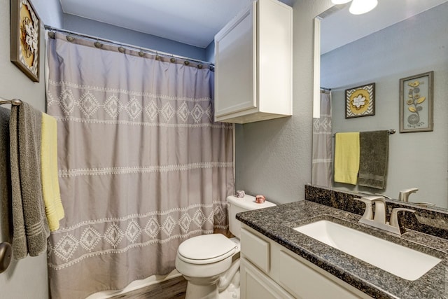 bathroom with toilet, a textured wall, a shower with shower curtain, and vanity