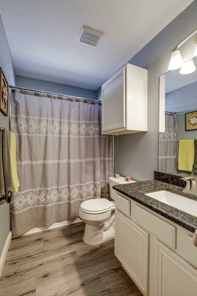 full bath with visible vents, a textured wall, toilet, wood finished floors, and vanity