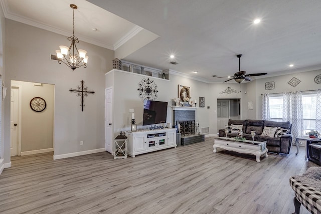 living room with crown molding, a fireplace with raised hearth, light wood-style floors, baseboards, and ceiling fan with notable chandelier