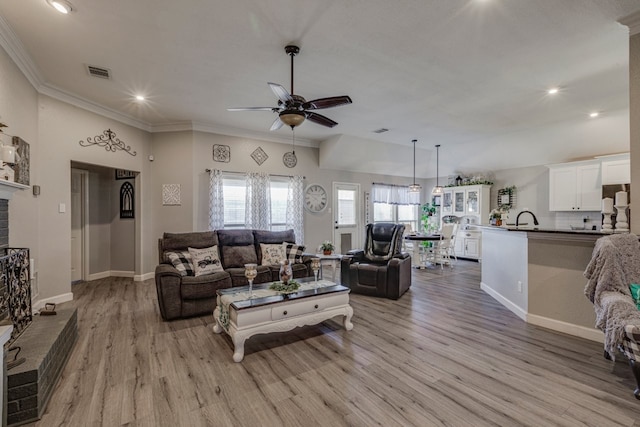 living area with visible vents, baseboards, wood finished floors, crown molding, and a brick fireplace