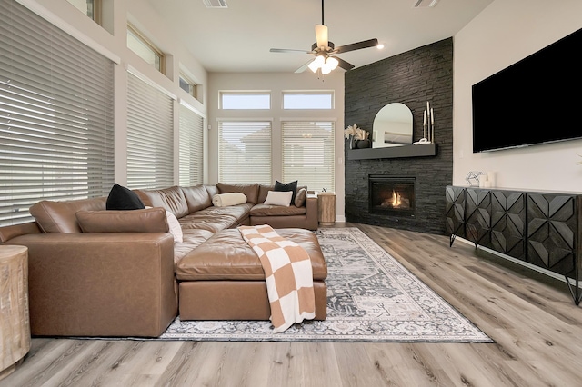 living room with a fireplace, visible vents, light wood-style flooring, a high ceiling, and ceiling fan